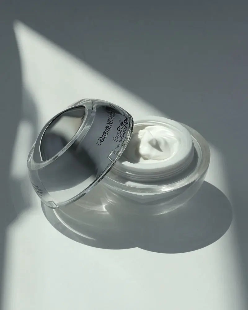 Silver spherical shaped skincare jar for the heaven bee peel on a white background. Jar is opened and lid is resting on the other half of the jar.