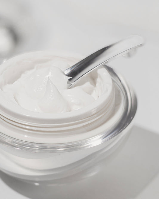 Jar of white cream with a silver spoon on a light gray background
