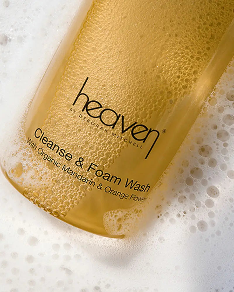 Close up of cleanse and foam product in the yellow bottle. The bottle is resting on a foamy, soapy background.