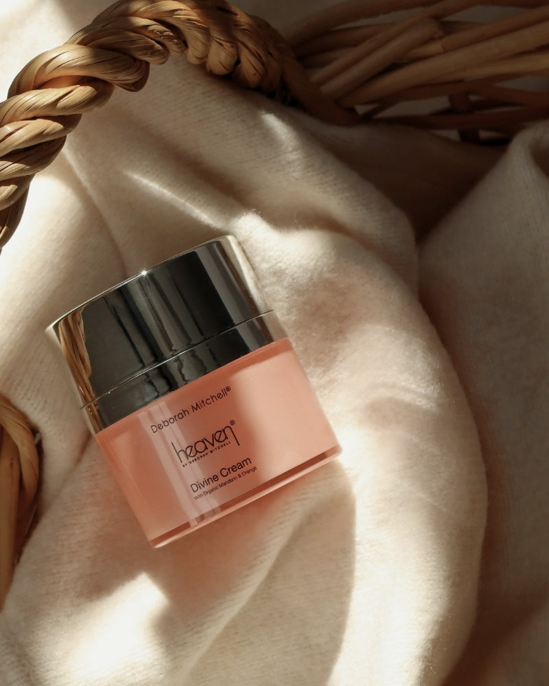 Pink skincare jar labeled 'heaven' on a soft beige blanket in a wicker basket