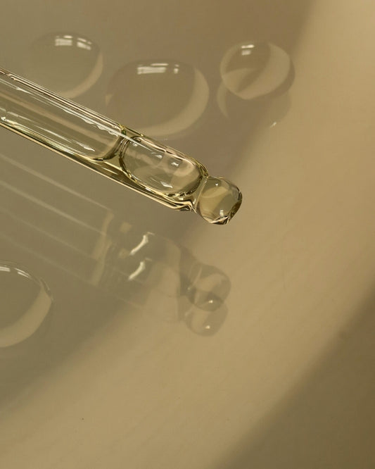 Close-up of a glass dropper with liquid on a reflective surface