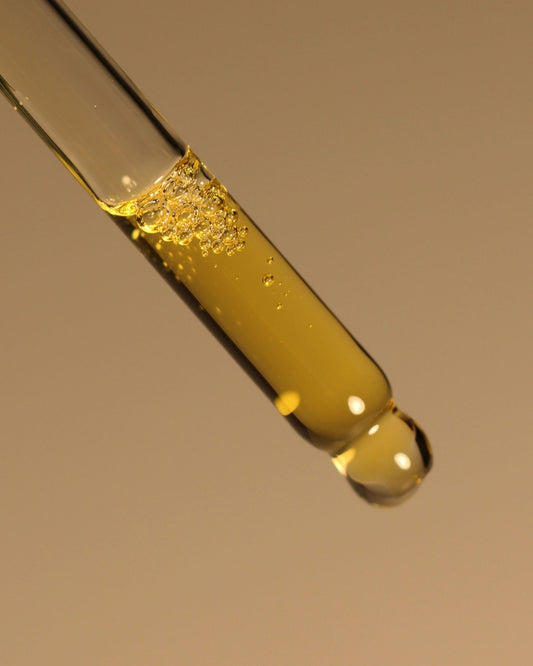 Close-up of a dropper with yellow liquid against a brown background