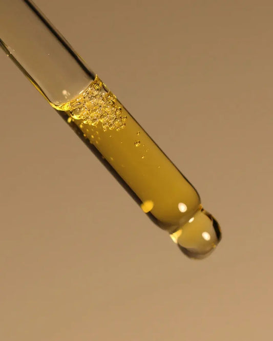 Close-up of a dropper with yellow liquid against a brown background