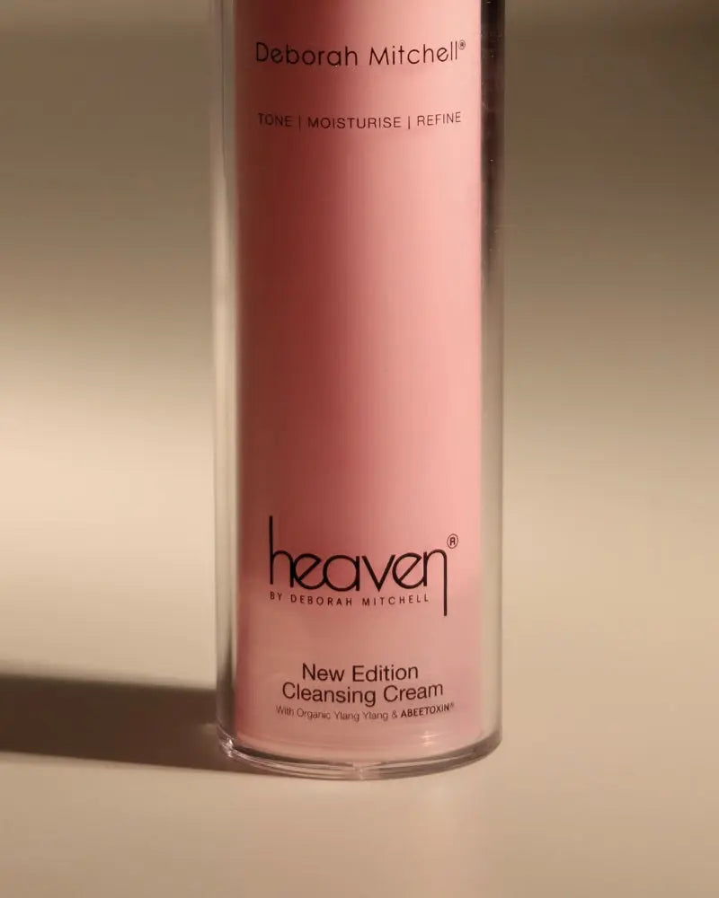 Pink bottle of New Edition Cleansing Cream. On beige background.