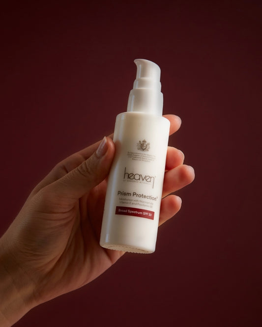 Hand holding a bottle of 'heaven' sun protection spray against a dark red background