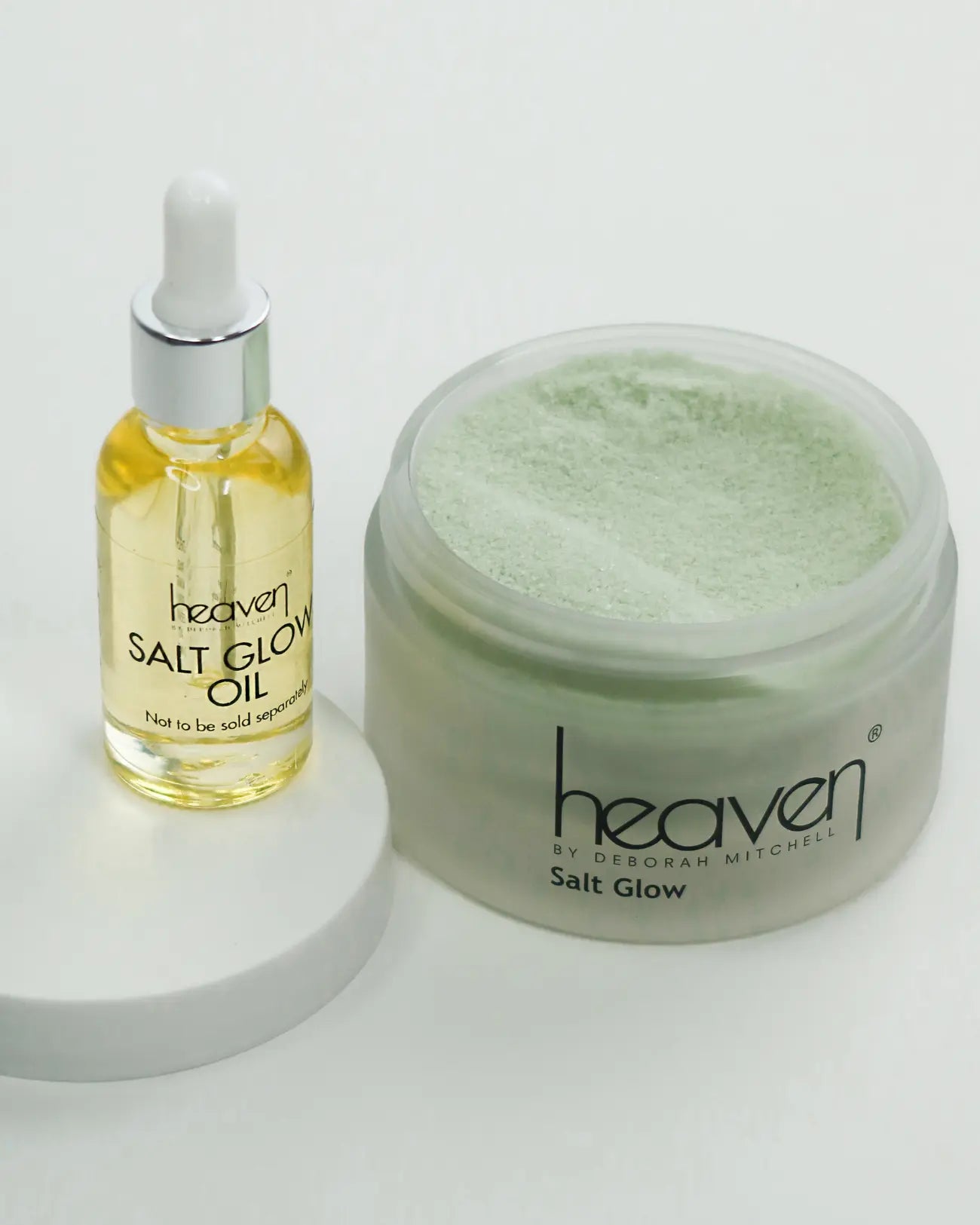 Heaven Salt Glow kit: clear jar of green salt scrub and a dropper bottle of yellow oil on a white stand.