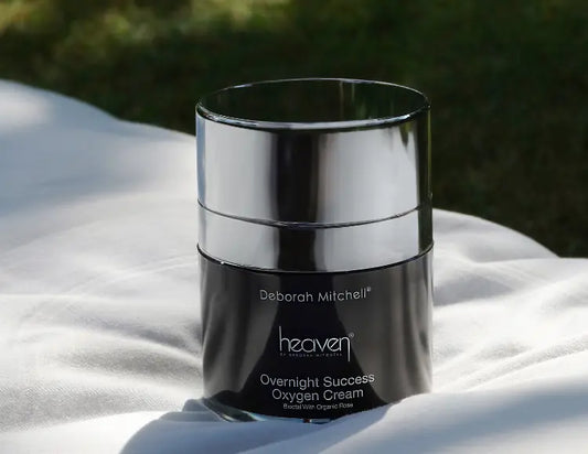 A black jar of overnight success oxygen cream with a silver lid. The product is on a white sheet with grass in the background.